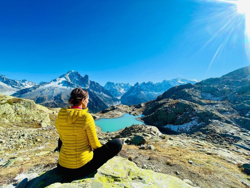 Céline en position de lotus, méditant lors d’une randonnée en haute montagne en Haute-Savoie, illustrant l’importance de la connexion à la nature, le retour à soi, et la respiration consciente.