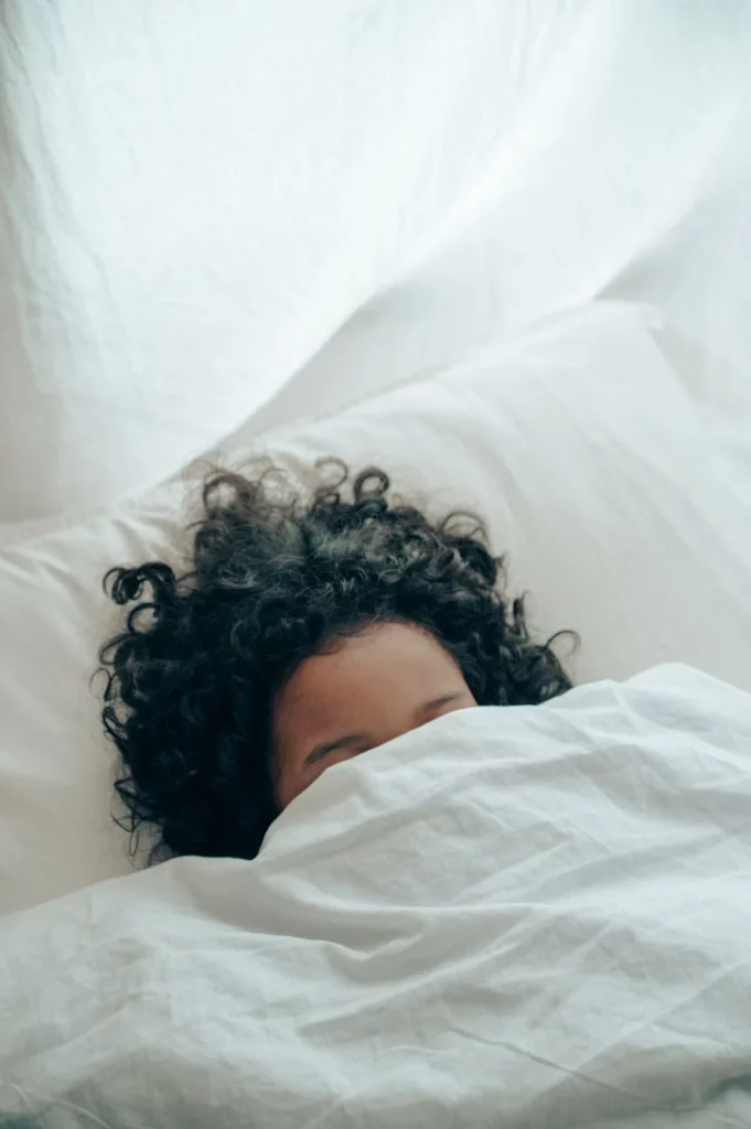 Femme se reposant sous une couette après un soin bien-être, illustrant l’importance de se détendre pour prolonger les bienfaits du soin. Information pratique: Massage à Domicile Côte Bleue, les conditions à réunir.