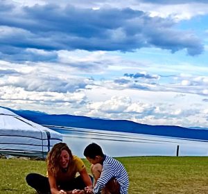 Céline dessinant avec un petit garçon en Mongolie, assis au bord d’un lac, dans un environnement naturel et isolé.