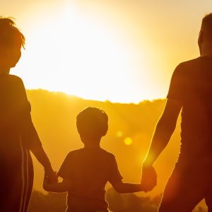 “Photo d’un couple tenant par la main leur enfant, face à un coucher de soleil paisible, symbolisant la sérénité et la connexion familiale offerte par le soin ‘Family Zen’ d’Immersive Expérience.”